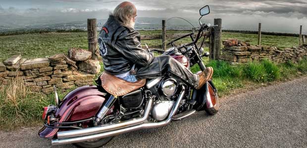 Man on a motorcycle with patches on the back of his leather jacket