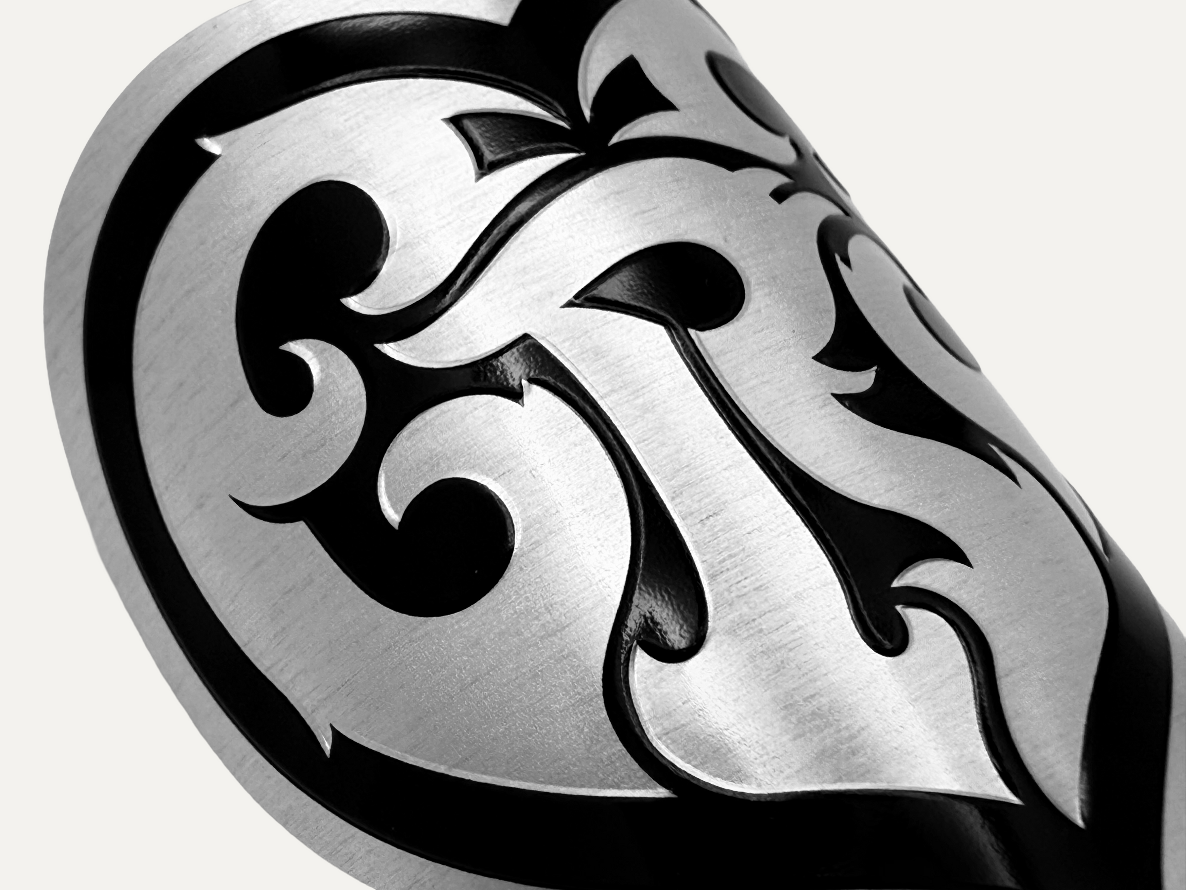 Ornate embossed metallic scrollwork label applied to a curved black product surface