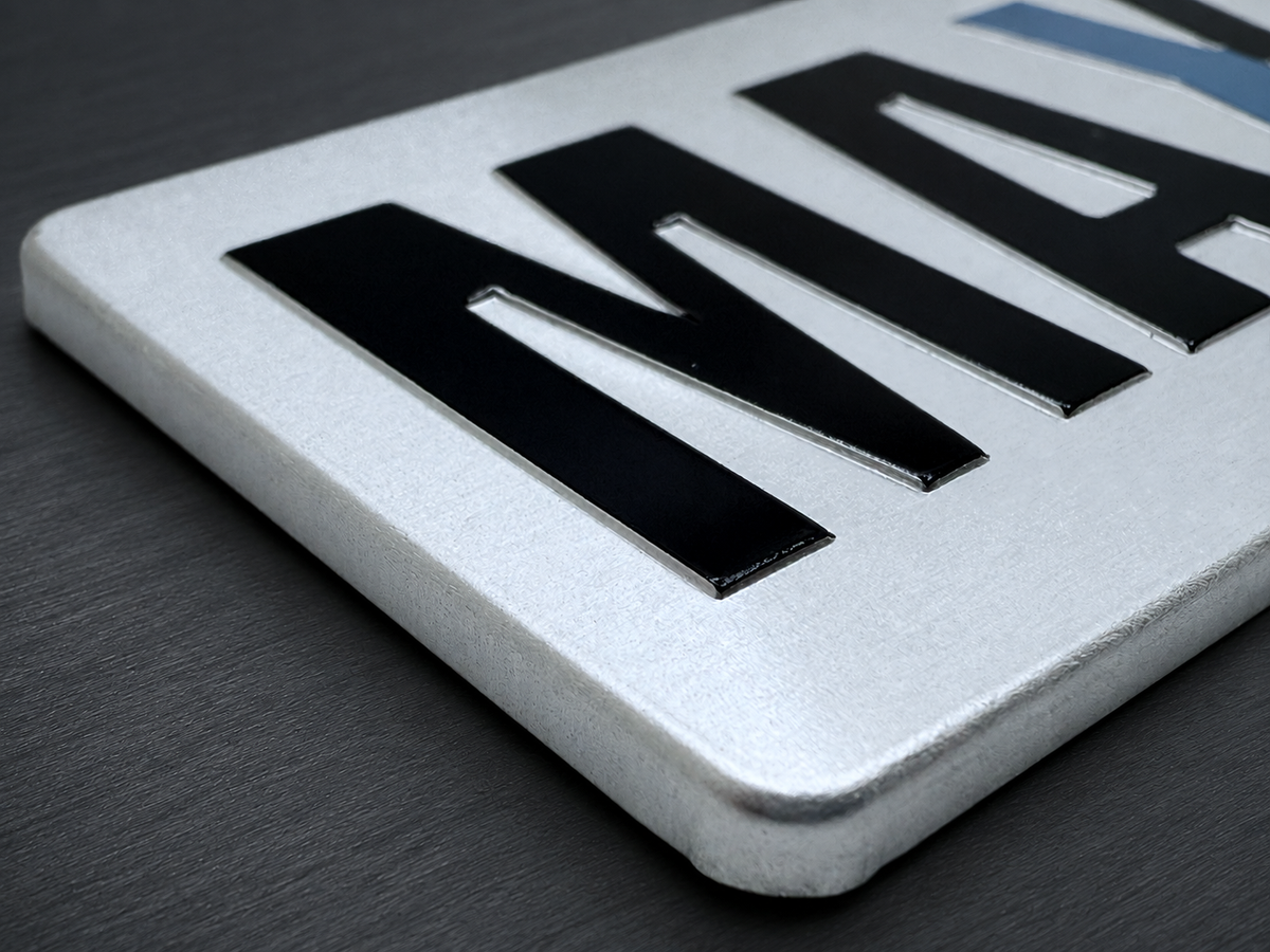 Close-up of raised black lettering on a formed aluminum badge showing depth and edge geometry.