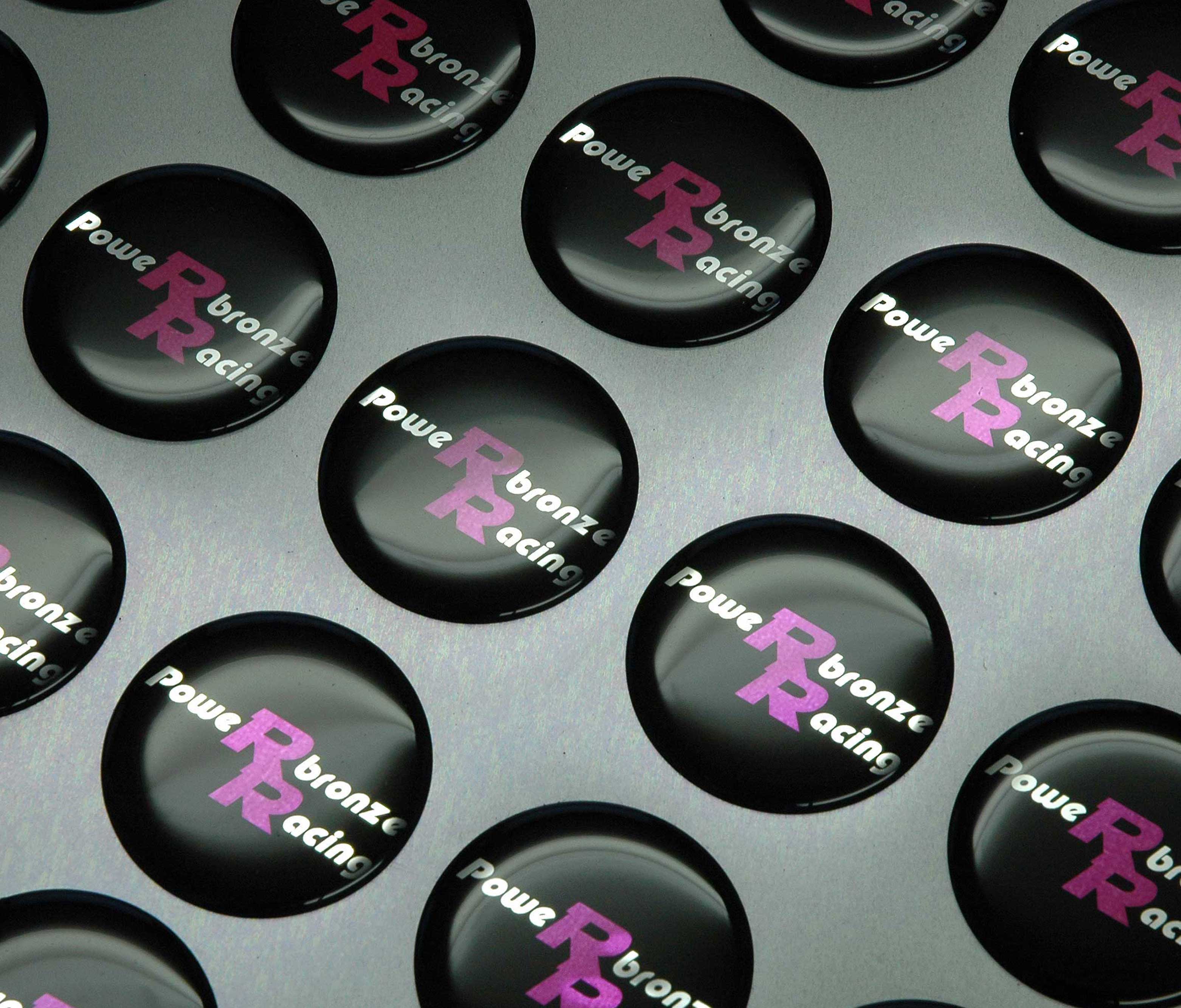 Black domed badges with silver and purple screen printed lettering